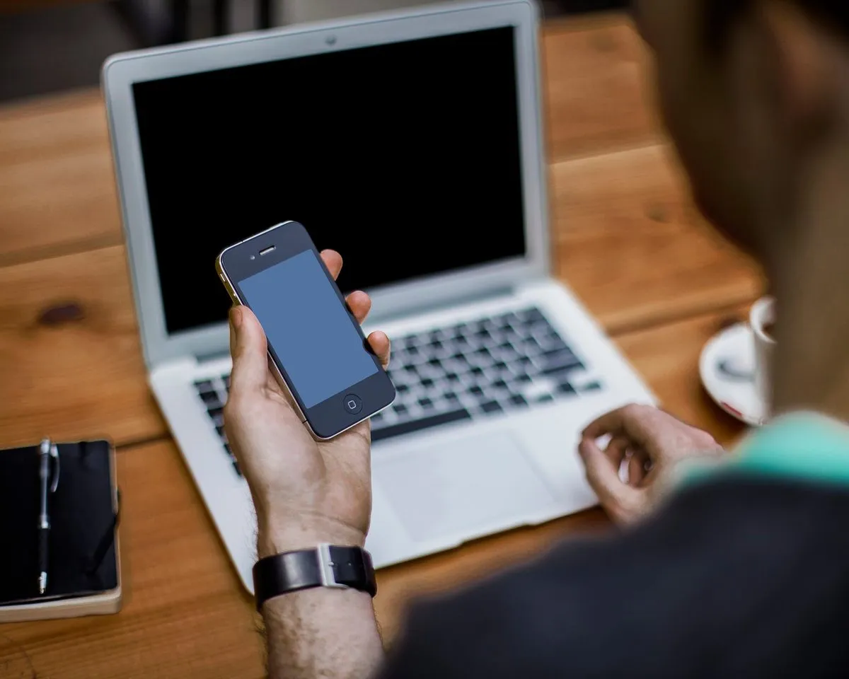 A man checking his insurance account on his phone in front of a laptop