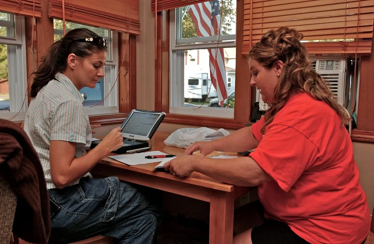 A damage inspector reviews flood-related receipts with a homeowner at her kitchen table