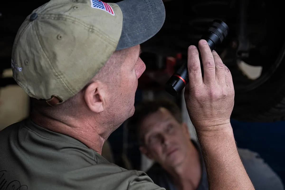 Mechanics inspecting the underside of a car on a lift in an auto repair shop