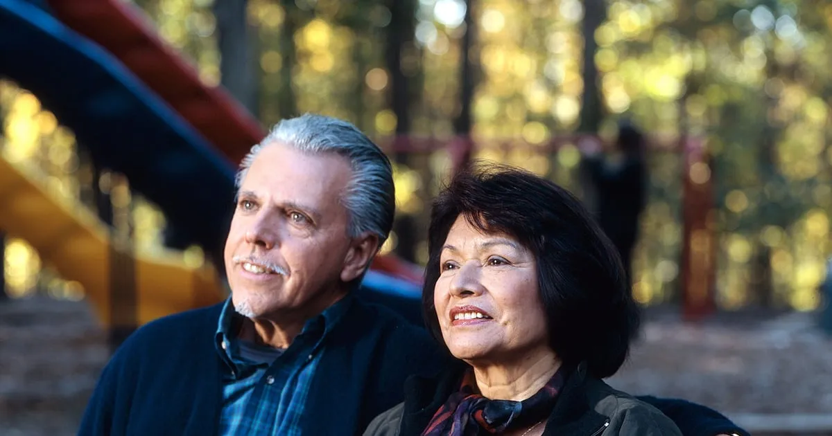 An older couple sitting together on a park bench on an autumn day