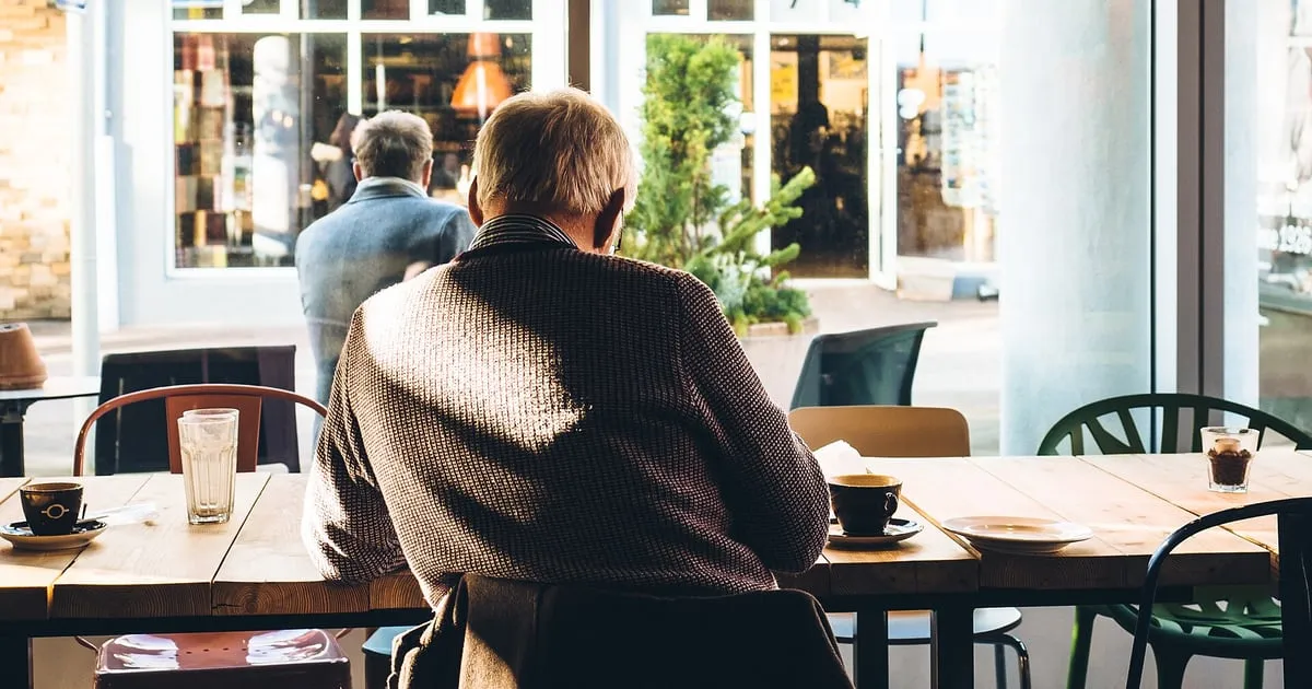 An older man sitting at a café table reading by a sunny window