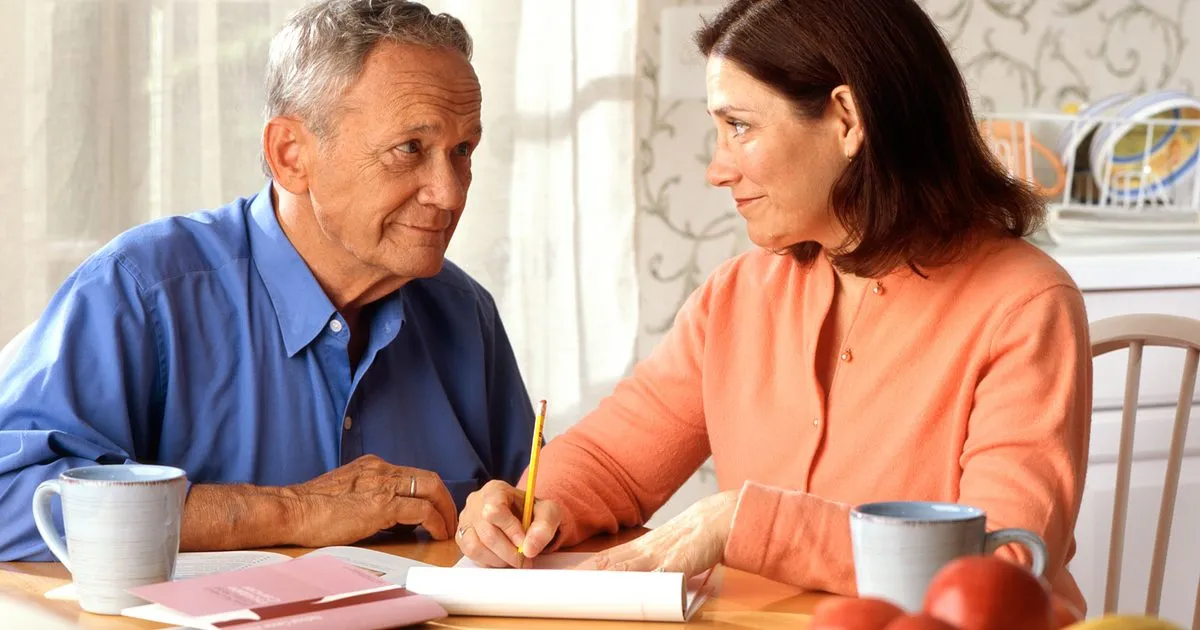 An older man and his adult daughter reviewing Medicare plan paperwork together at the kitchen table