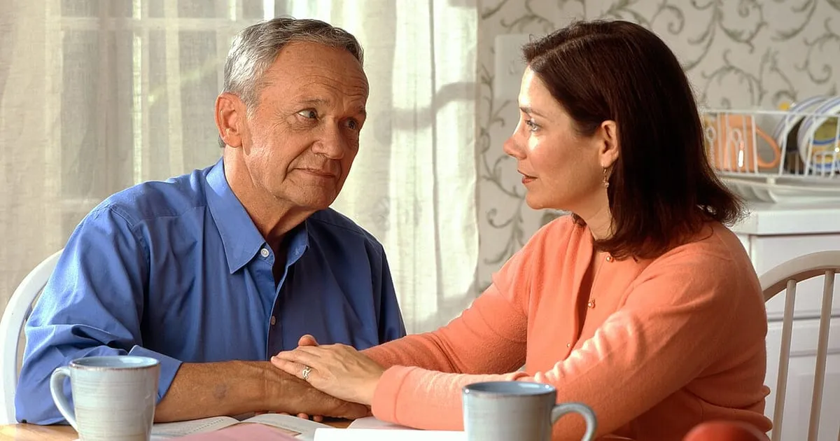 An older man and a younger woman sitting at a kitchen table going over paperwork together