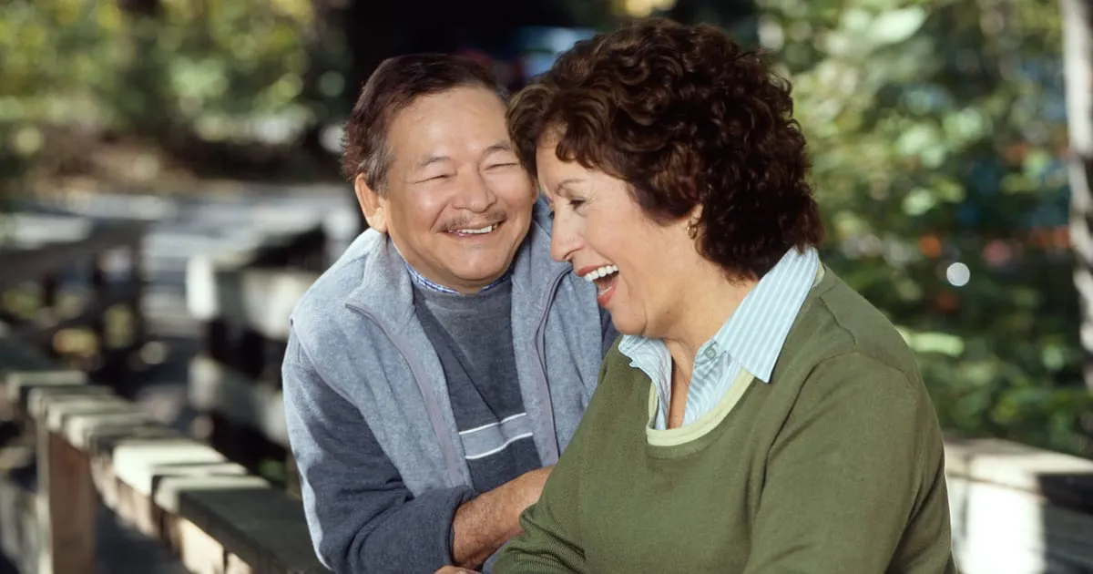 A smiling older couple talking together outdoors on a wooden footbridge