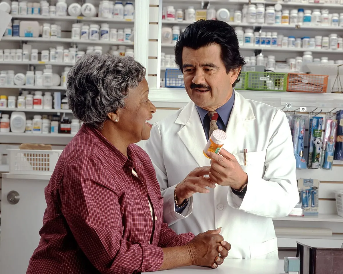 An older woman reviewing a prescription with her pharmacist at a pharmacy counter