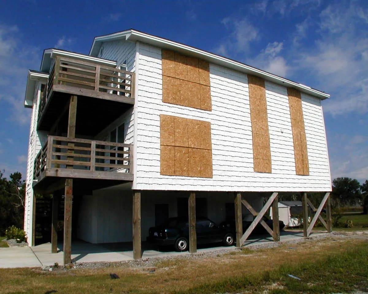 Workers boarding up the windows of a raised coastal home with plywood before a hurricane