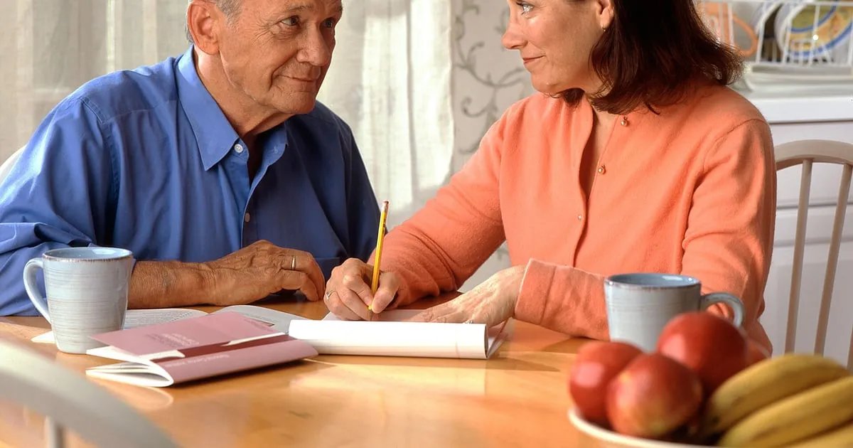 An older man and his adult daughter reviewing paperwork together at a kitchen table