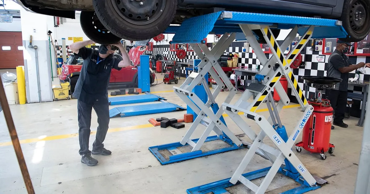 A mechanic inspecting the underside of a car raised on a lift in a repair shop