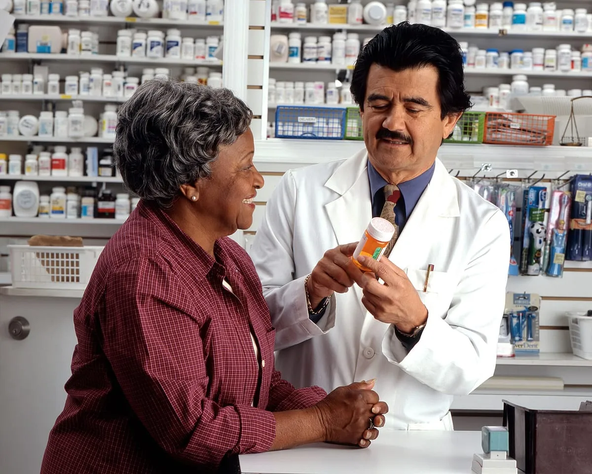 An older woman listens as a pharmacist explains her prescription at a pharmacy counter